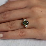 close up of hand wearing large green sapphire engagement ring with round diamonds
