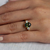 close up of hand wearing large green sapphire engagement ring with round diamonds