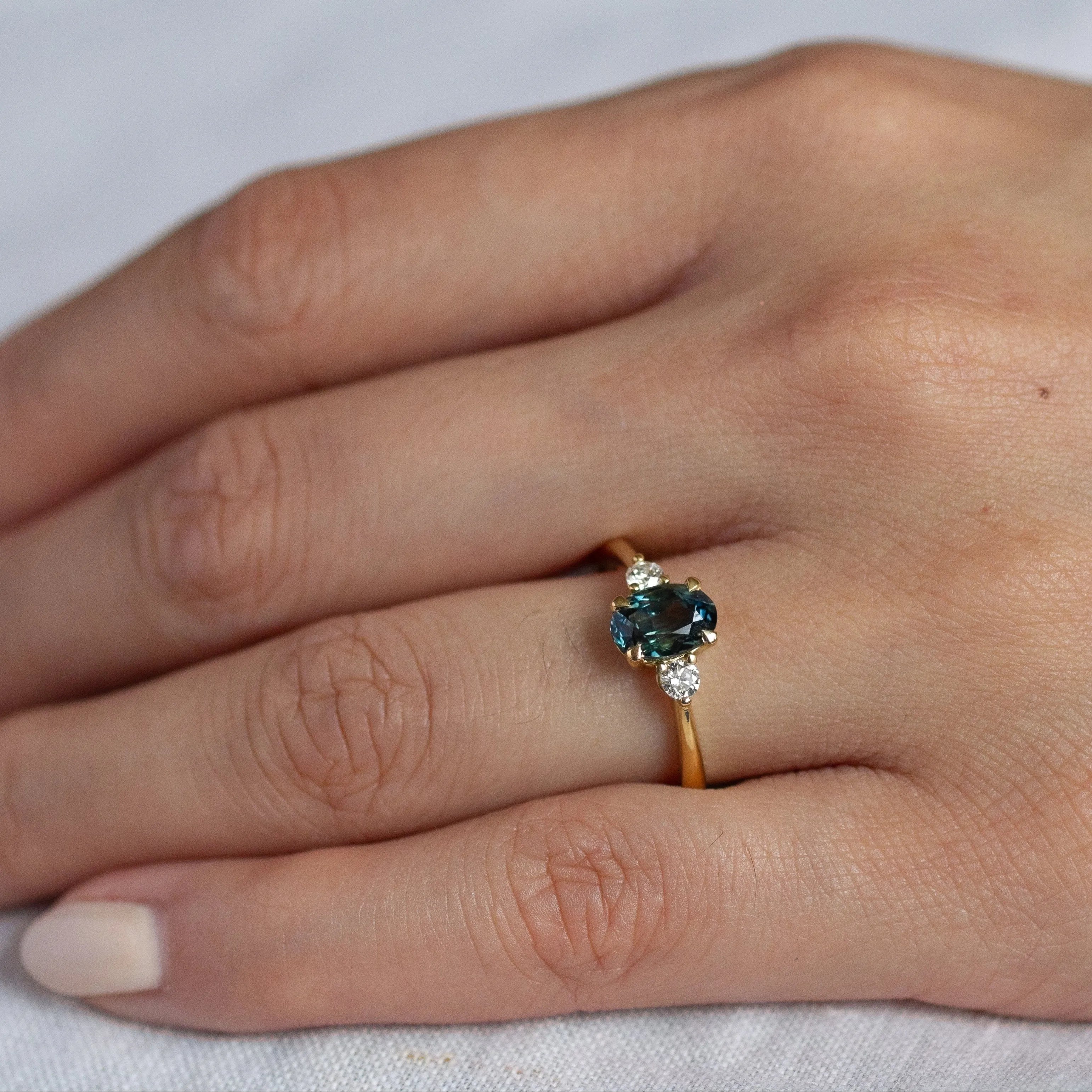 hand wearing green and bllue sapphire engagement ring with round diamonds and gold band