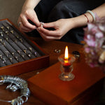 hands comparing two engagement rings, sat infront of an open box of engagement rings