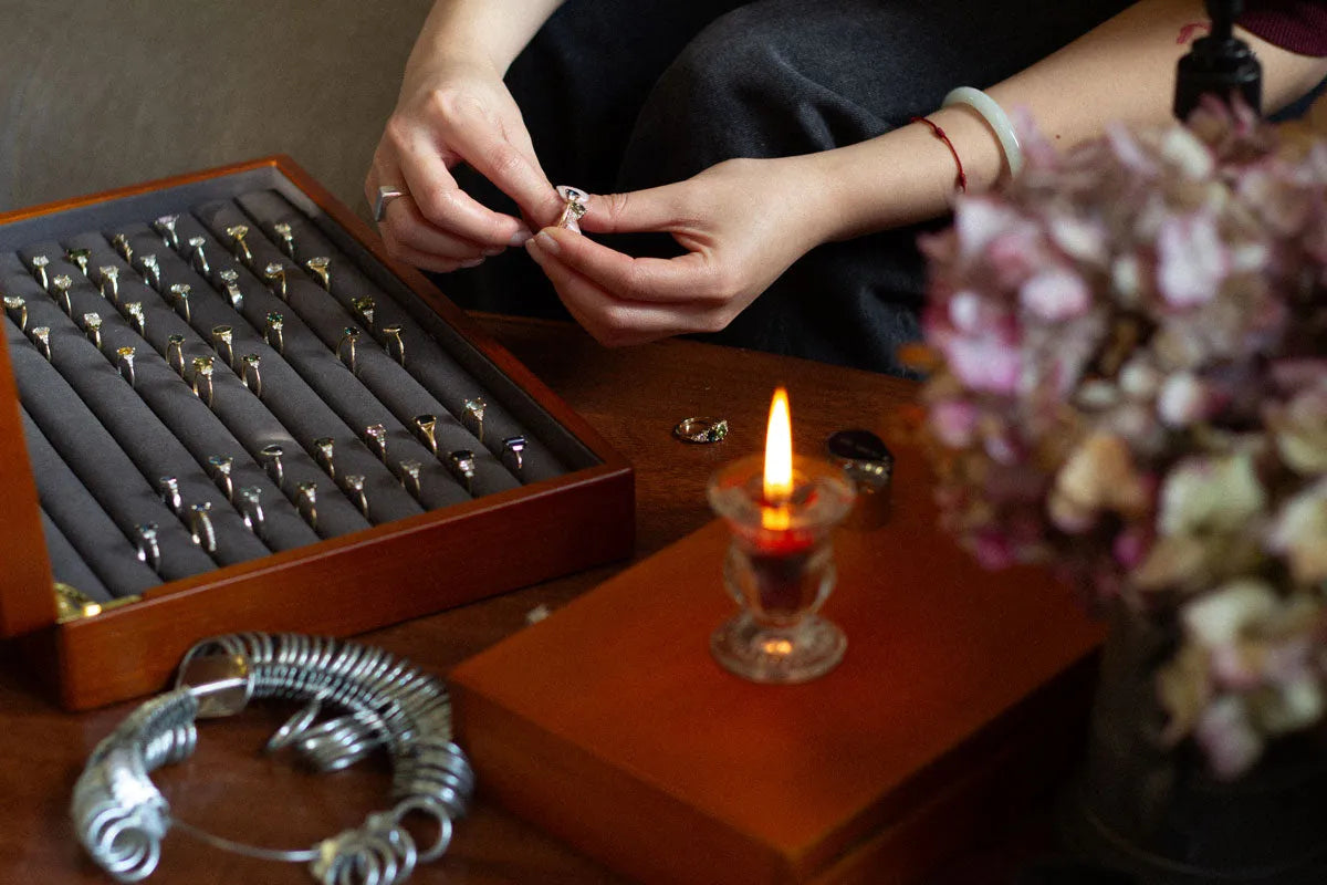 hands comparing two engagement rings, sat infront of an open box of engagement rings