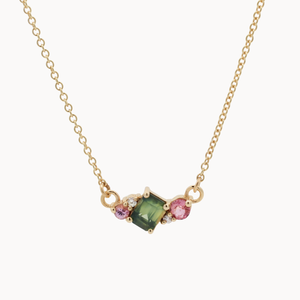 Necklace with a green gemstone and pink stones on a gold chain against a white background