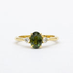 Gold ring with a forest green sapphire and smaller diamonds on a white background