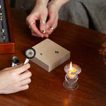 hand holding magnifying tool holding a blue sapphire, with another set of hands holding an engagement ring