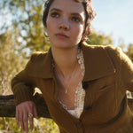 Woman wearing a brown coat with a lace top and gold acorn necklace outdoors