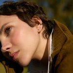 woman with short hair outside wearing brown cardigan, gold ear cuff and diamond studs