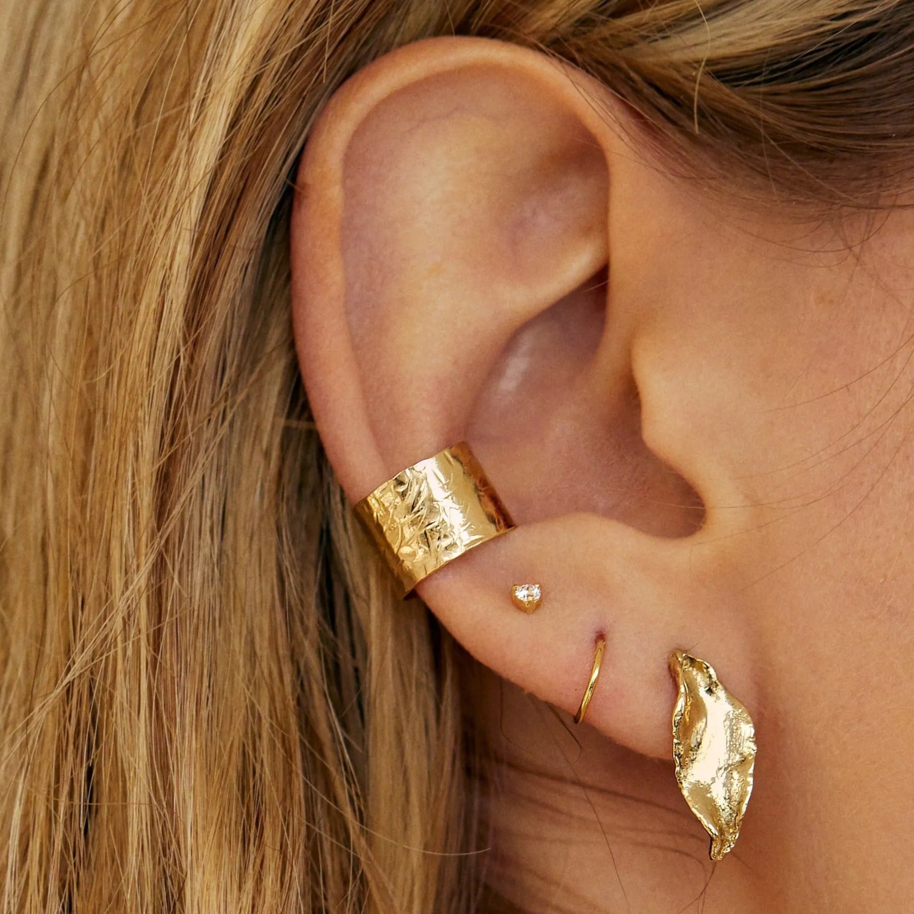 ear wearing gold earrings including hammered ear cuff and leaf studs