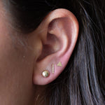 Brunette model wearing pebble, bar and triangle gold stud earrings