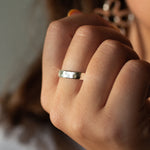 Close-up of a hand wearing a silver hammered ring with a blurred background