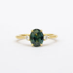 Gold ring with a teal green sapphire and smaller diamonds on a white background