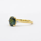 Trilogy engagement ring with a green teal gemstone on a white background