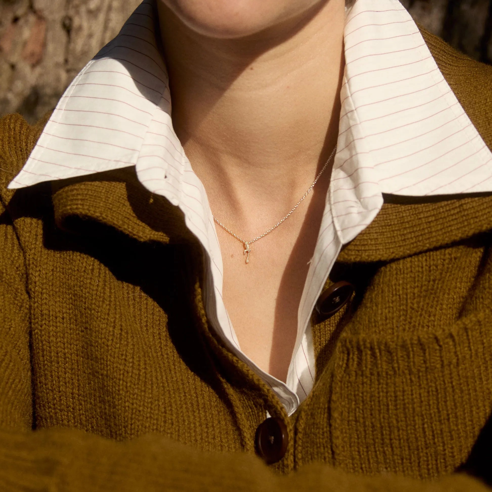 Close-up of a person wearing a brown sweater over a white shirt with a number necklace.