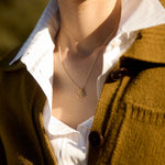 Person wearing a mustard-colored cardigan over a white shirt with a necklace featuring a three number pendants.