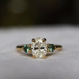 large diamond oval engagement ring with green sapphires and blurred background