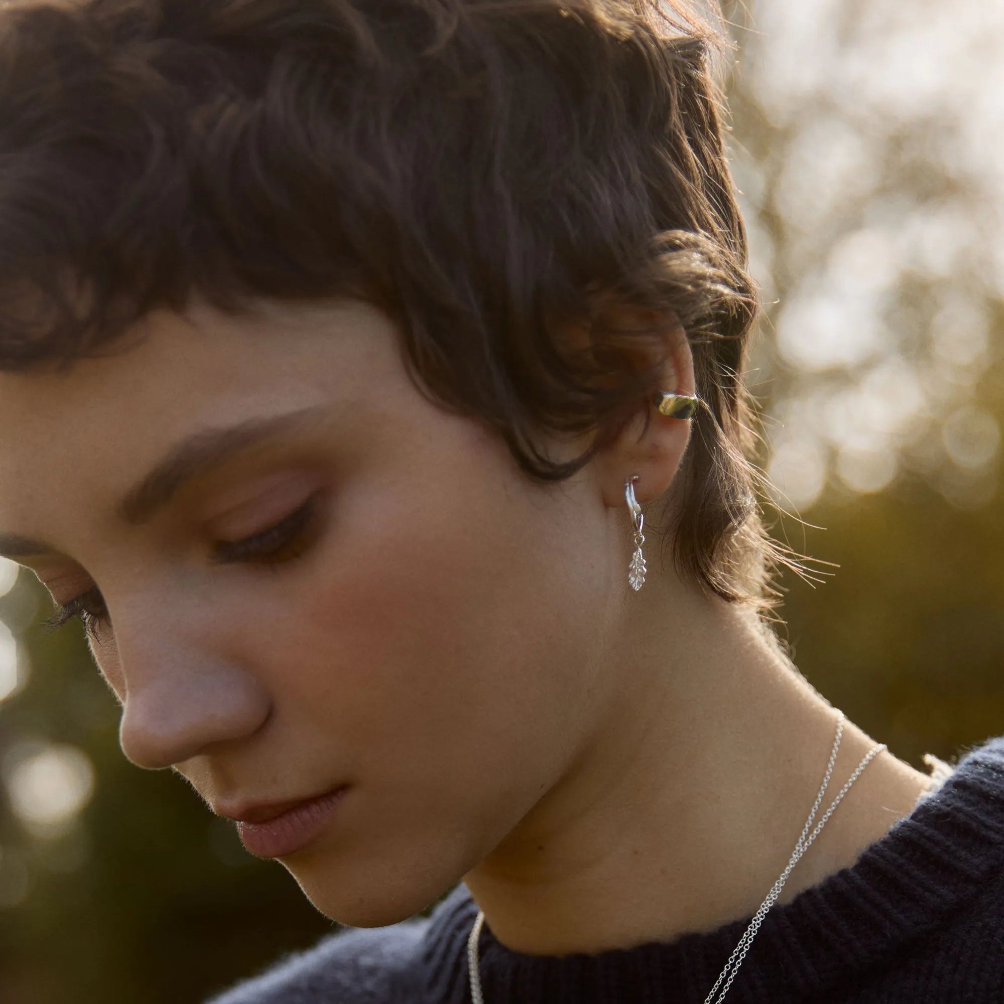 Close-up of a person wearing silver oak earrings with a blurred natural background