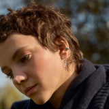Close-up of a person wearing oak leaf earrings and silver ear cuff with a blurred leafy background
