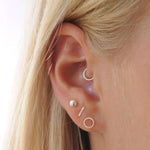 Close-up of an ear with multiple silver earrings on a neutral background