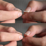 Close-up of hands demonstrating how to open and close the small silver helix hoop earrings against a neutral background