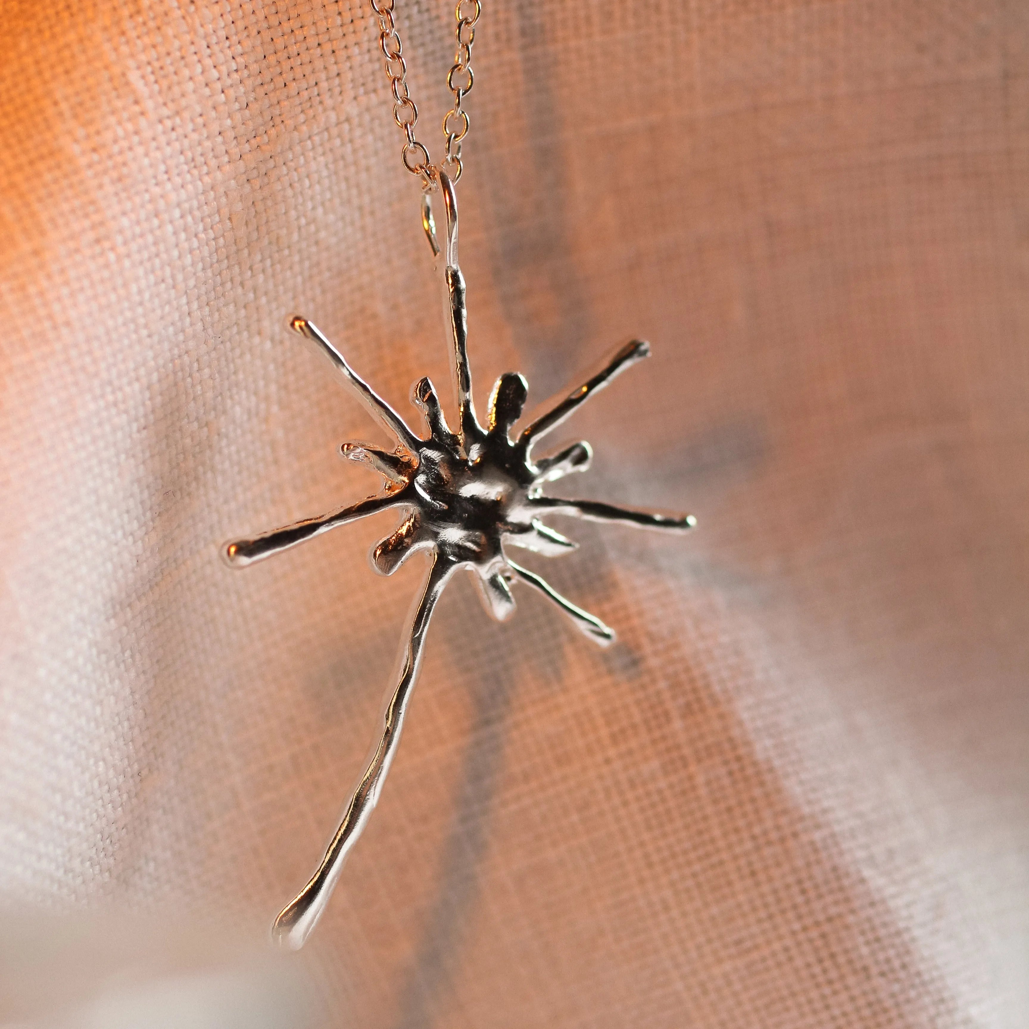 close up of silver dandelion pendant necklace with warm light and shadow