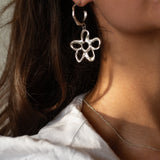 Close-up of a person wearing a silver flower-shaped earring and necklace.