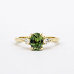 Gold ring with a green sapphire and smaller diamonds on a white background