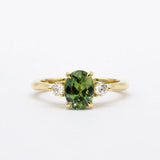 Gold ring with a green sapphire and smaller diamonds on a white background
