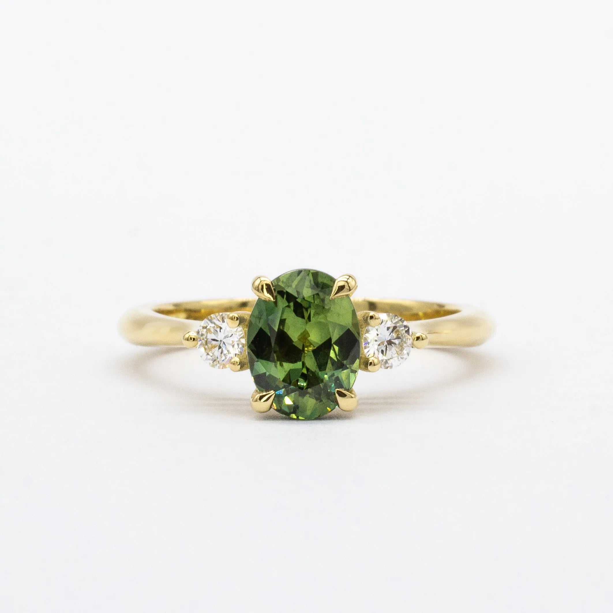 Gold ring with a green sapphire and smaller diamonds on a white background