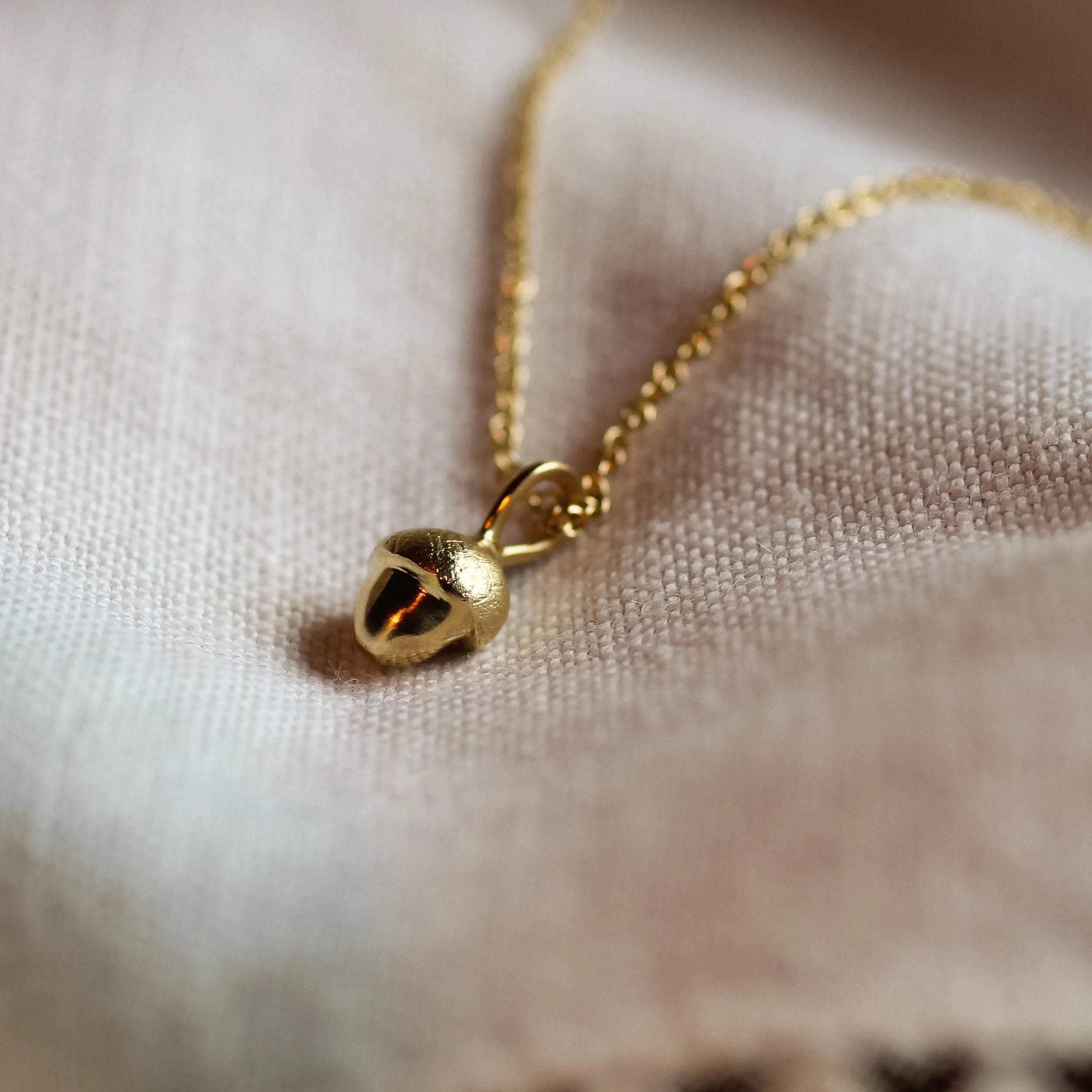 close up of 9ct gold acorn pendant necklace on neutral fabric