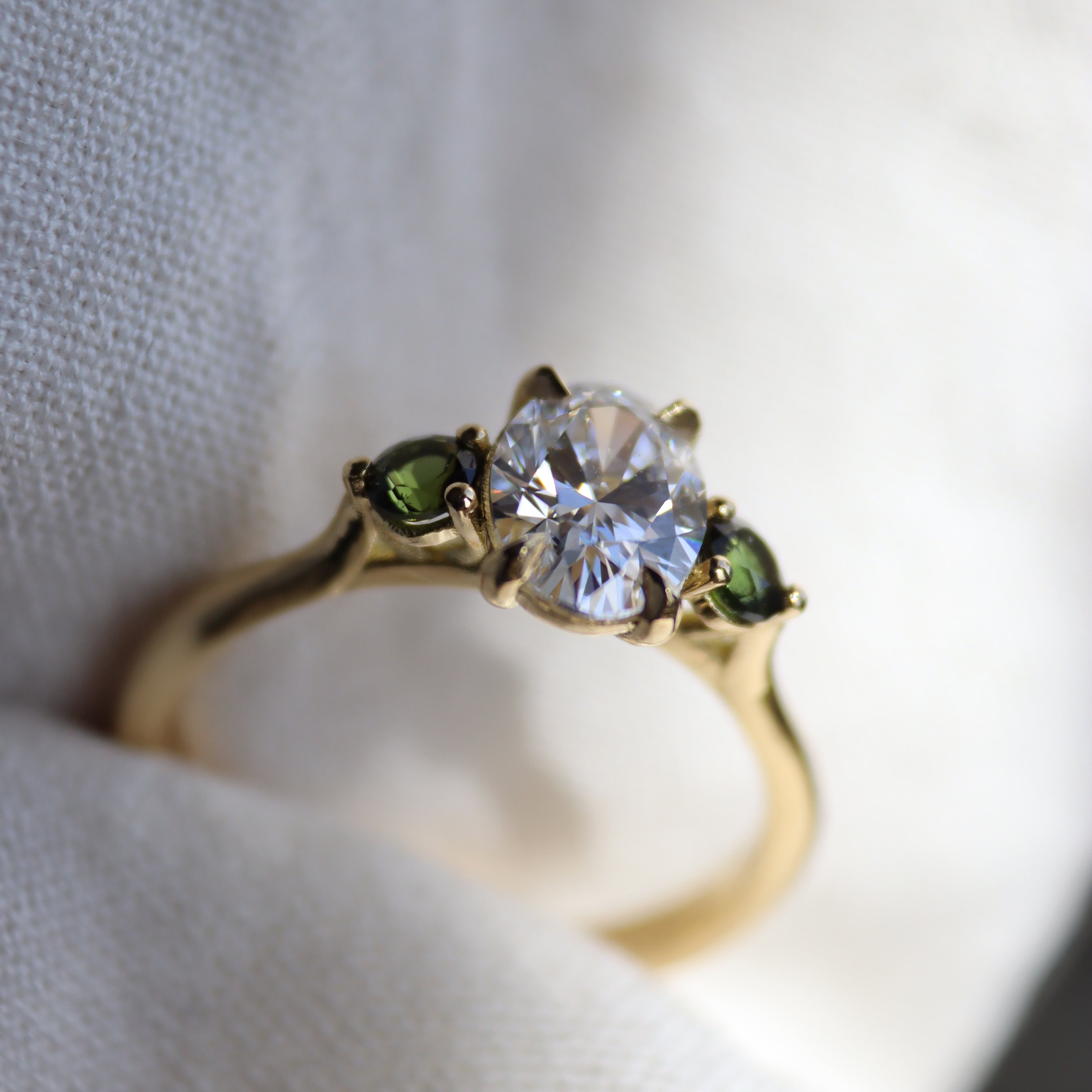 bespoke engagement ring with oval diamond and wo round green sapphires on gold band