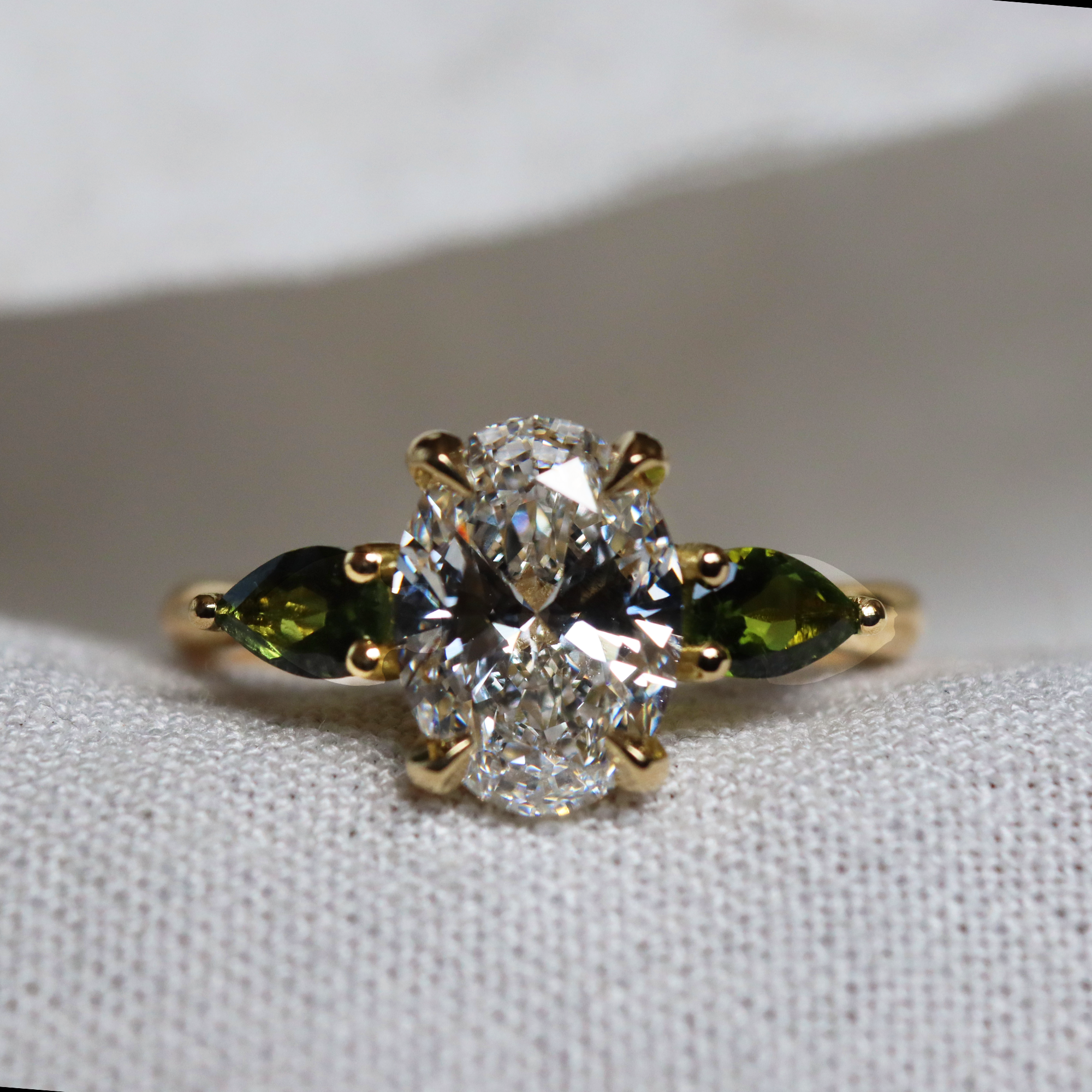 bespoke engagement ring with oval diamond and pear shaped green sapphires on yellow gold