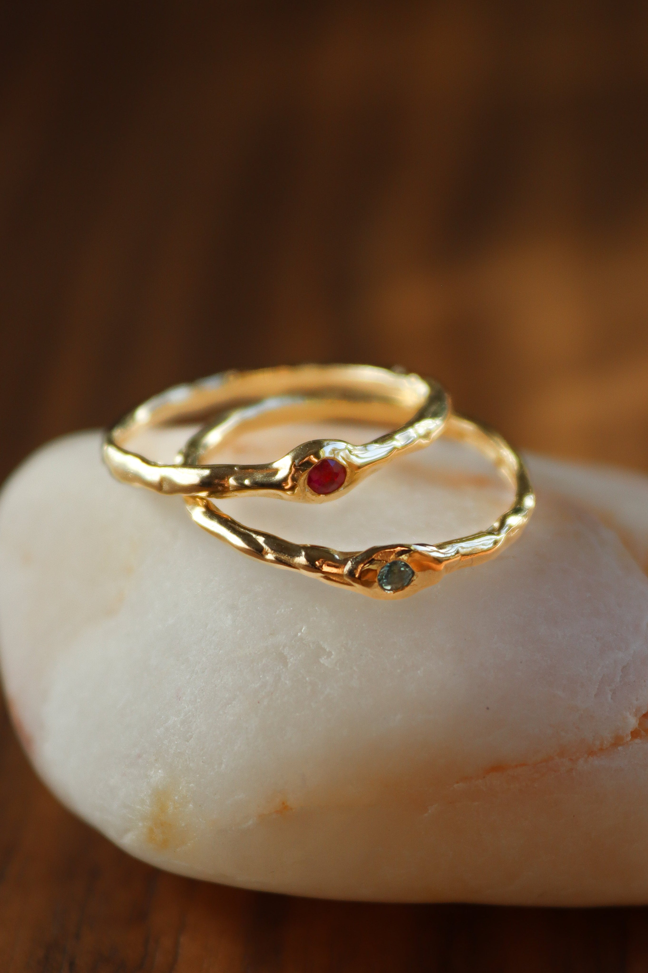 two organic gold rings with small red and green gemstones on a crystal