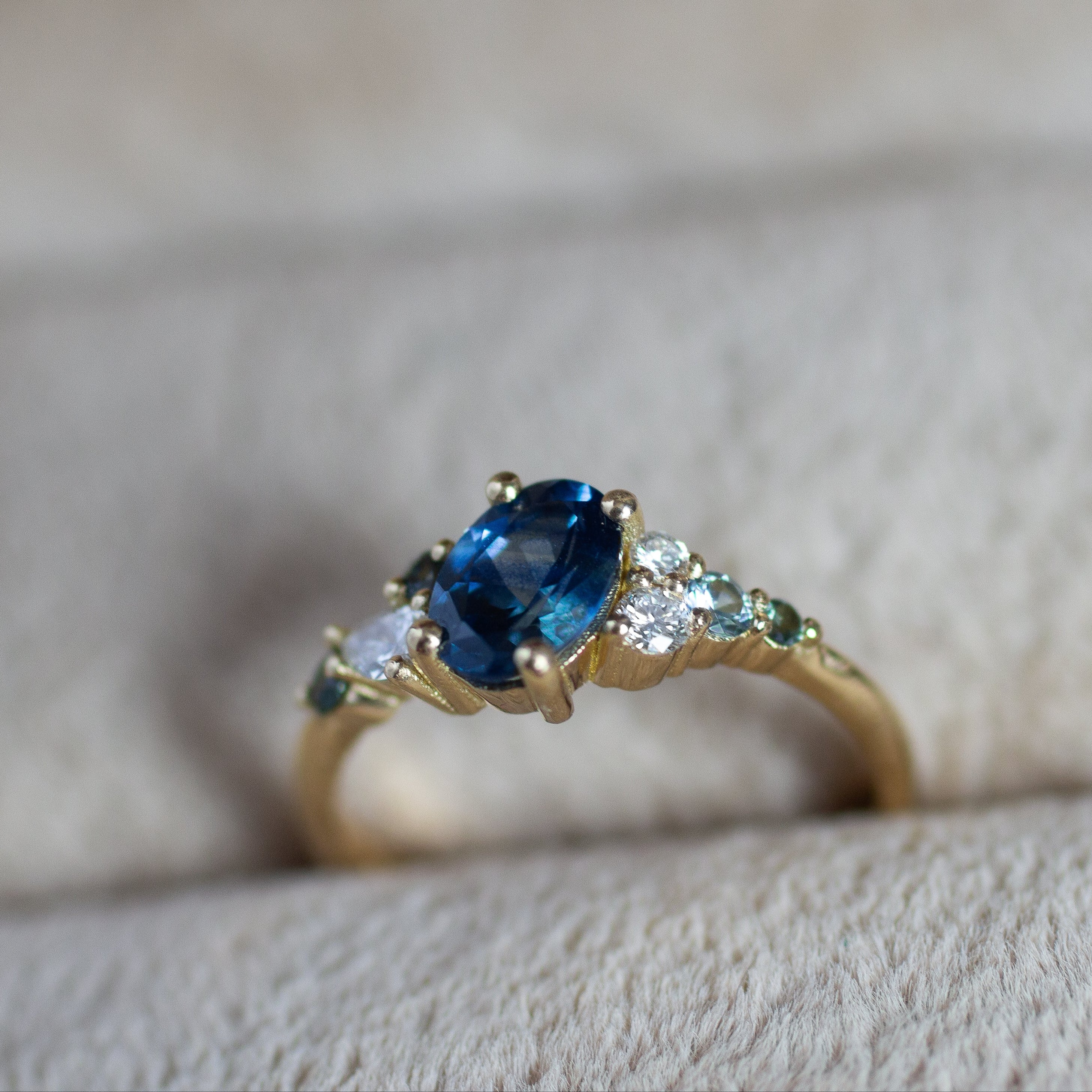 bespoke engagement ring with blue sapphire, round diamonds and small blue and teal round sapphires