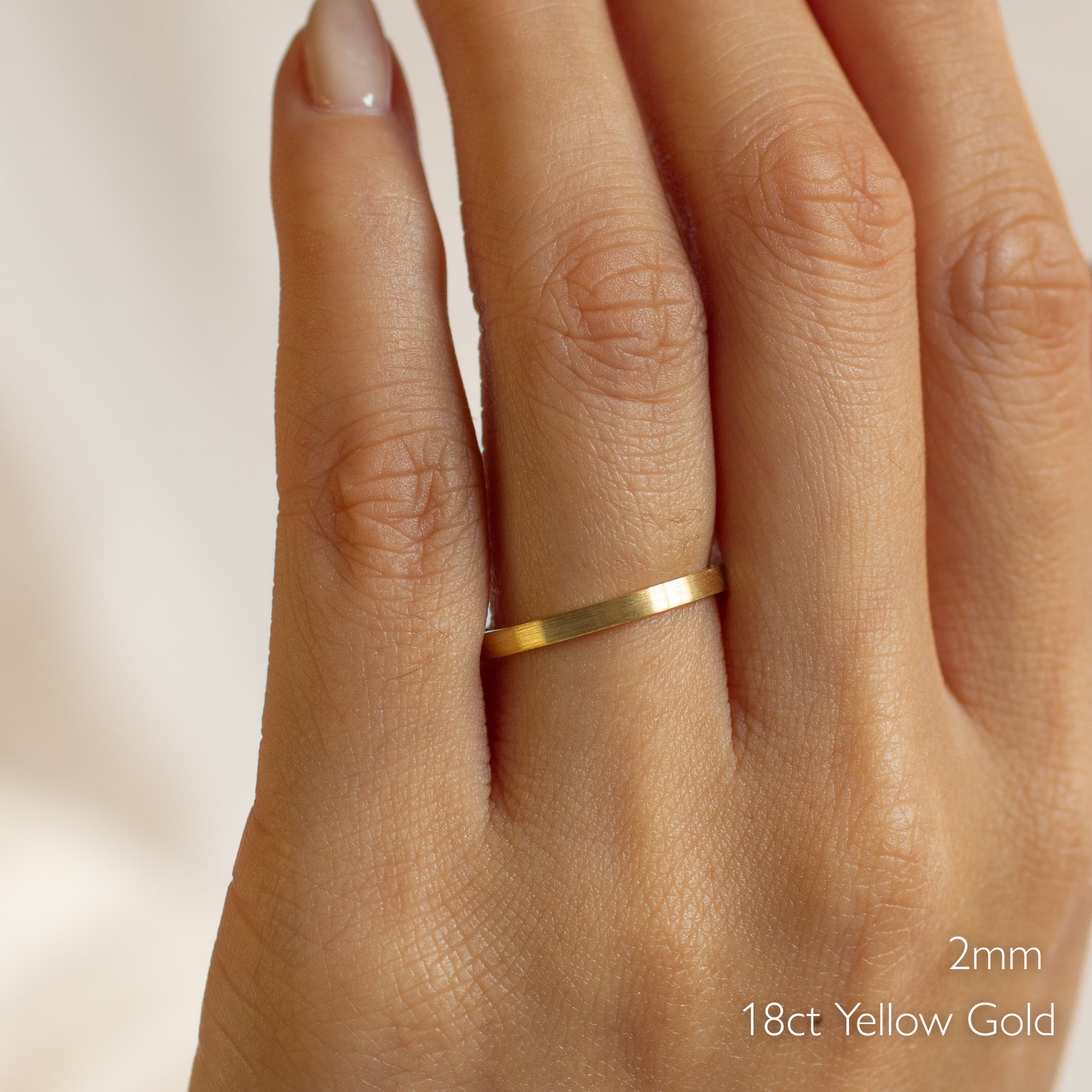 Gold brushed wedding ring in flat on a hand with '2mm 18ct Yellow Gold' text