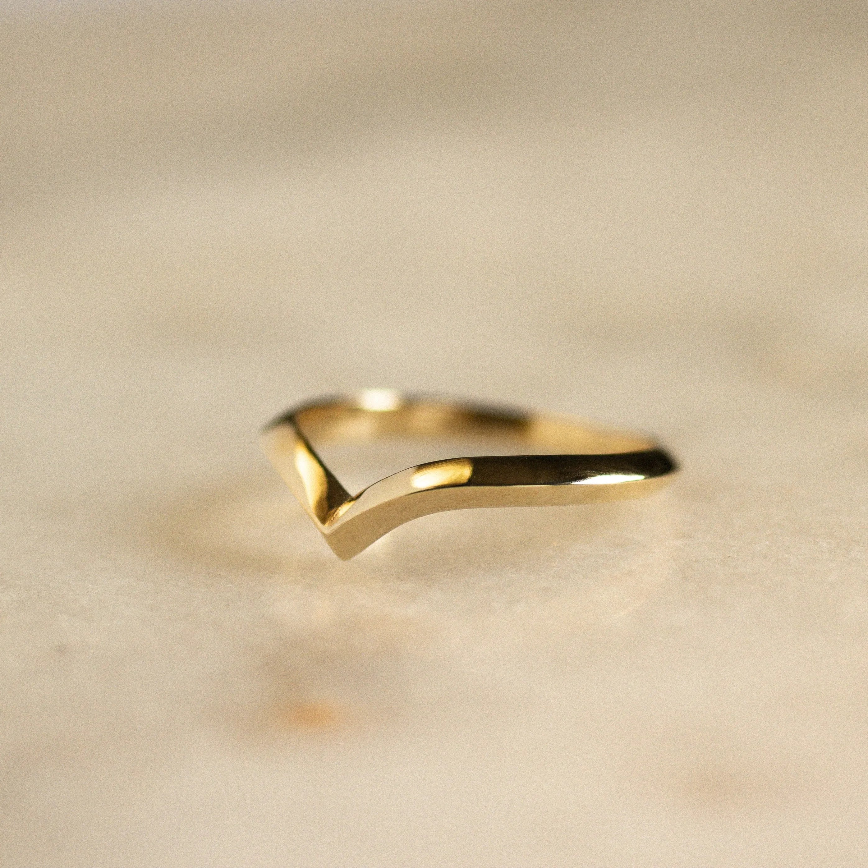v shaped gold wedding ring on marble surface in angular knife edge shape