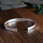 chunky silver bangle on wooden surface with leaves in the background