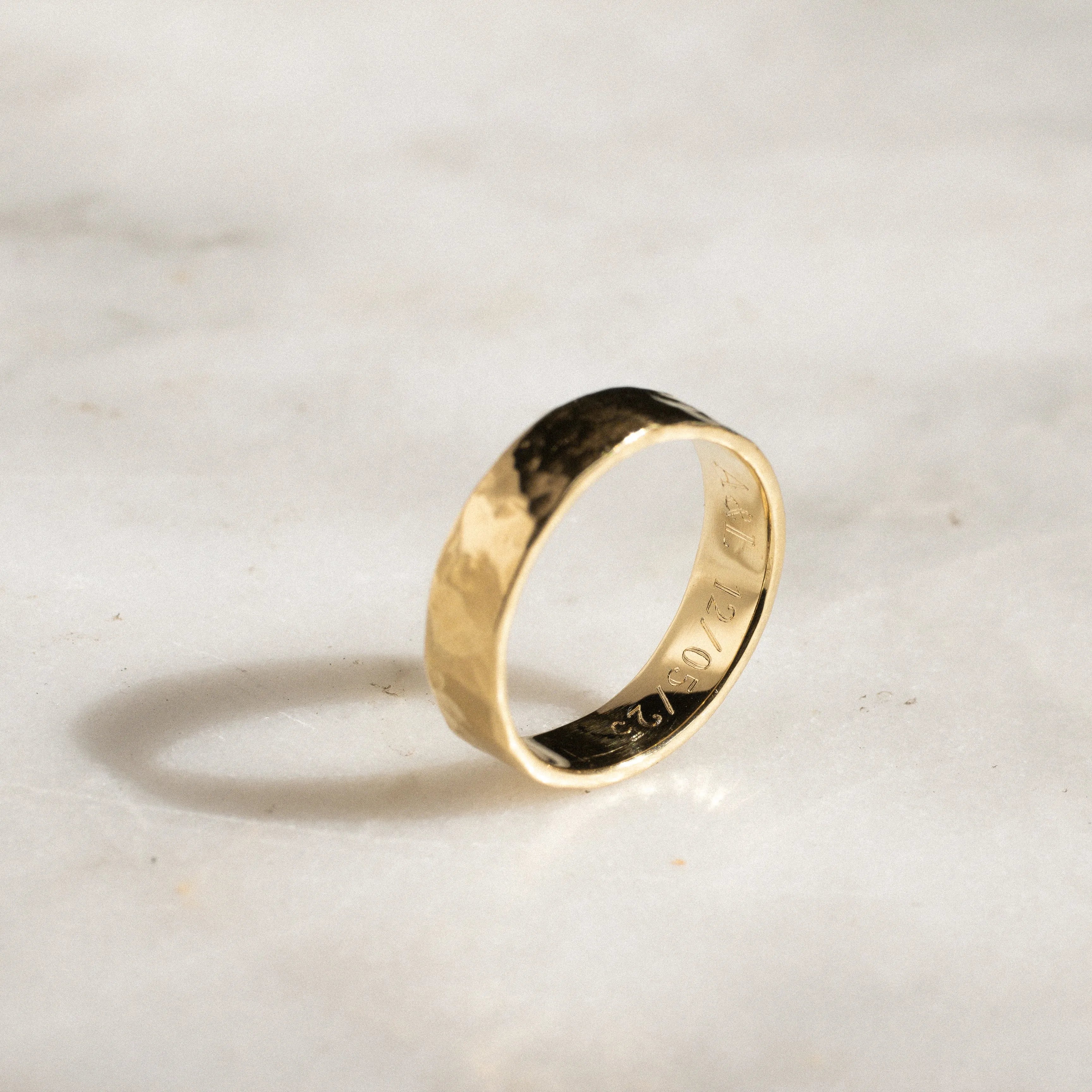 Gold ring on a light marble background with engraved date and initials
