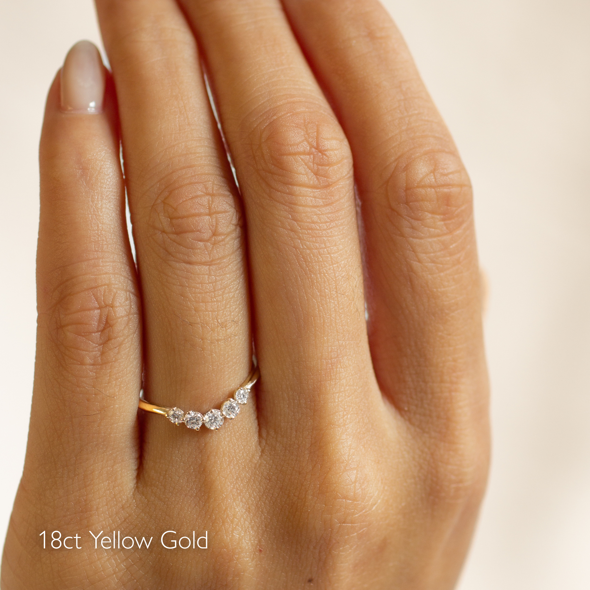 18ct yellow gold curved wedding ring with 5 diamonds on a hand against a beige background
