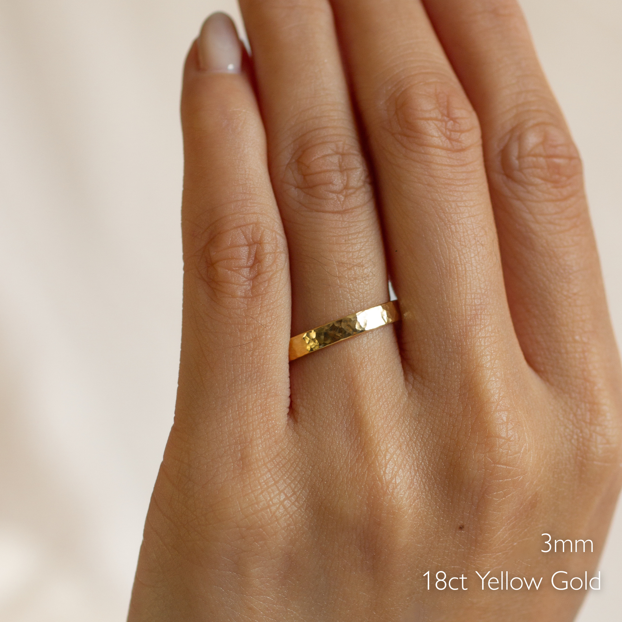 Gold chunky hammered flat wedding ring on a hand with '3mm 18ct Yellow Gold' text