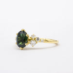 side view of gold engagement ring with a green sapphire and small diamonds on a white background