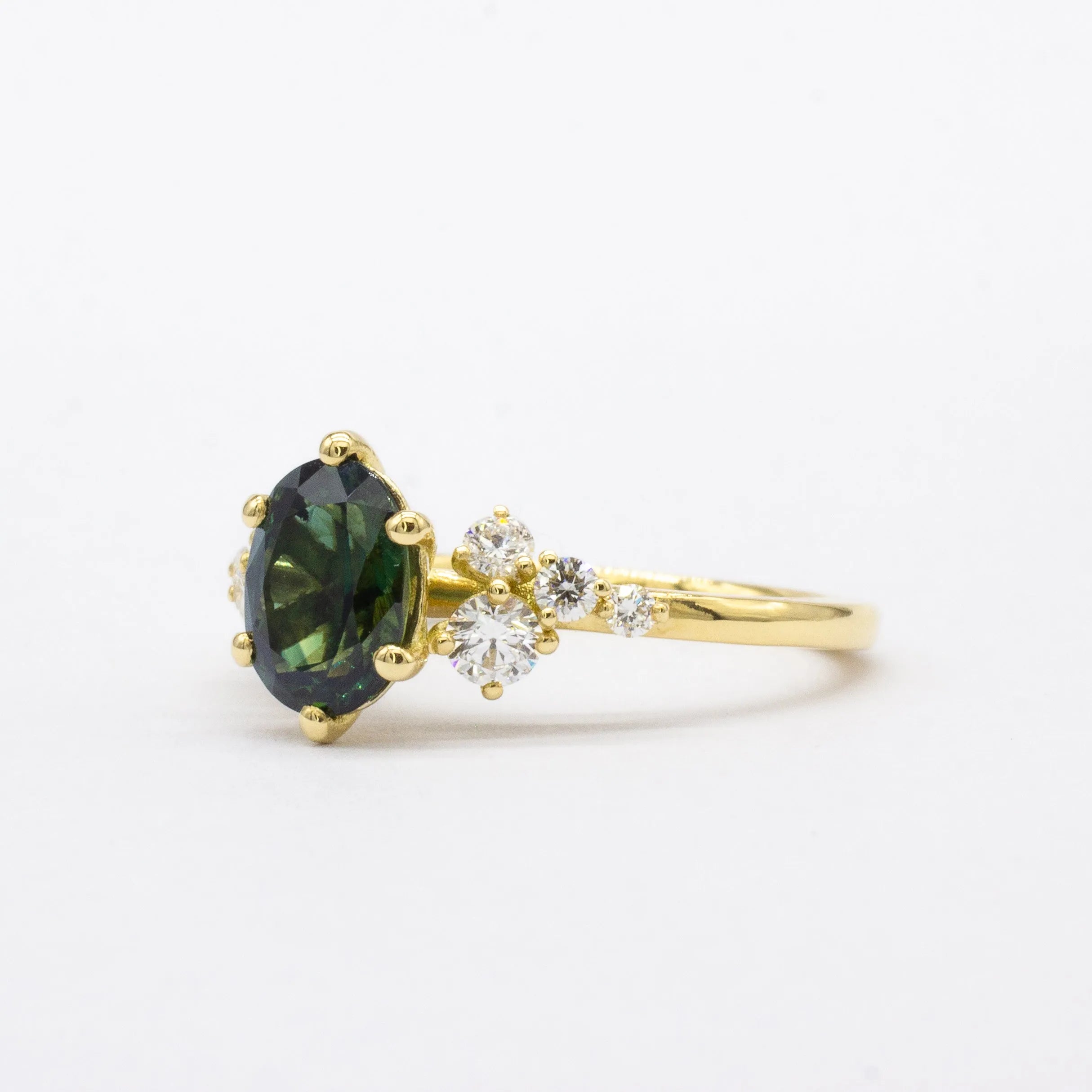 side view of gold engagement ring with a green sapphire and small diamonds on a white background
