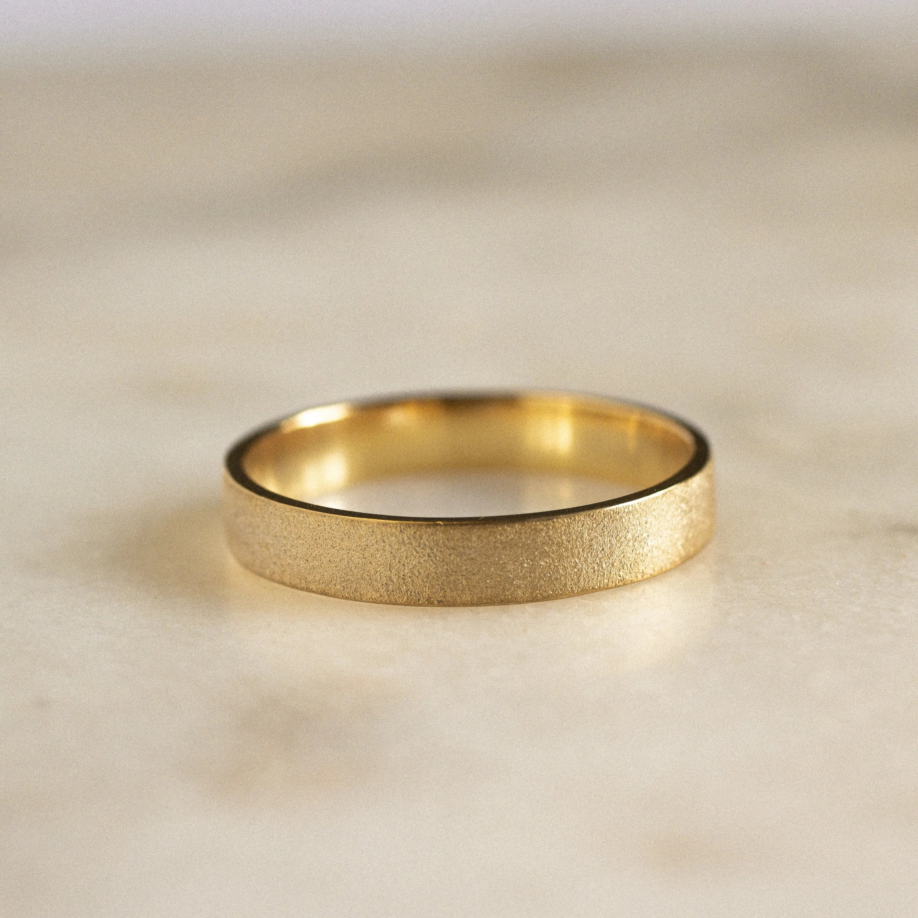 gold flat wedding ring with matte frosted finish on a marble surface
