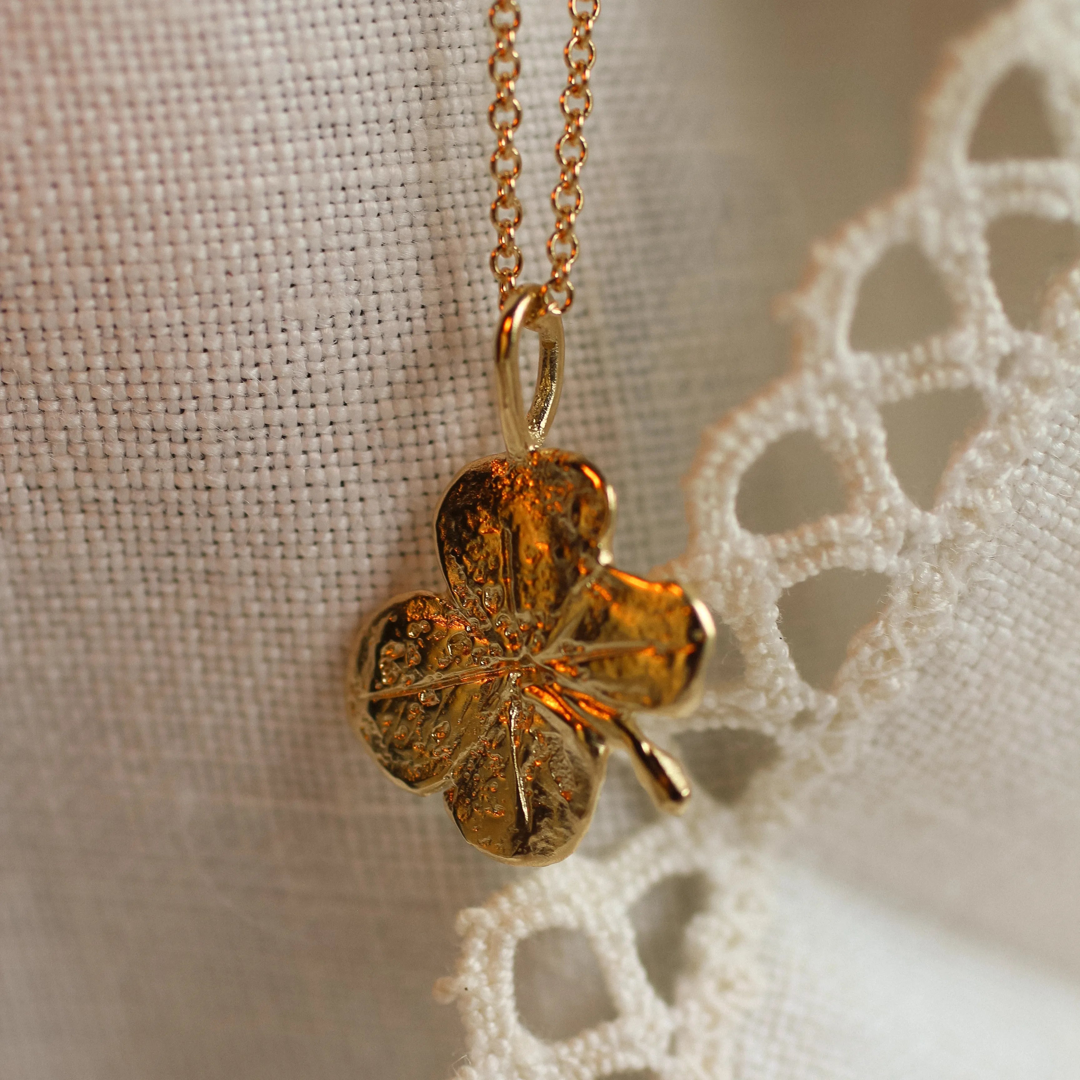 close up of solid gold pendant in 4 leaf clover shape on lace fabric