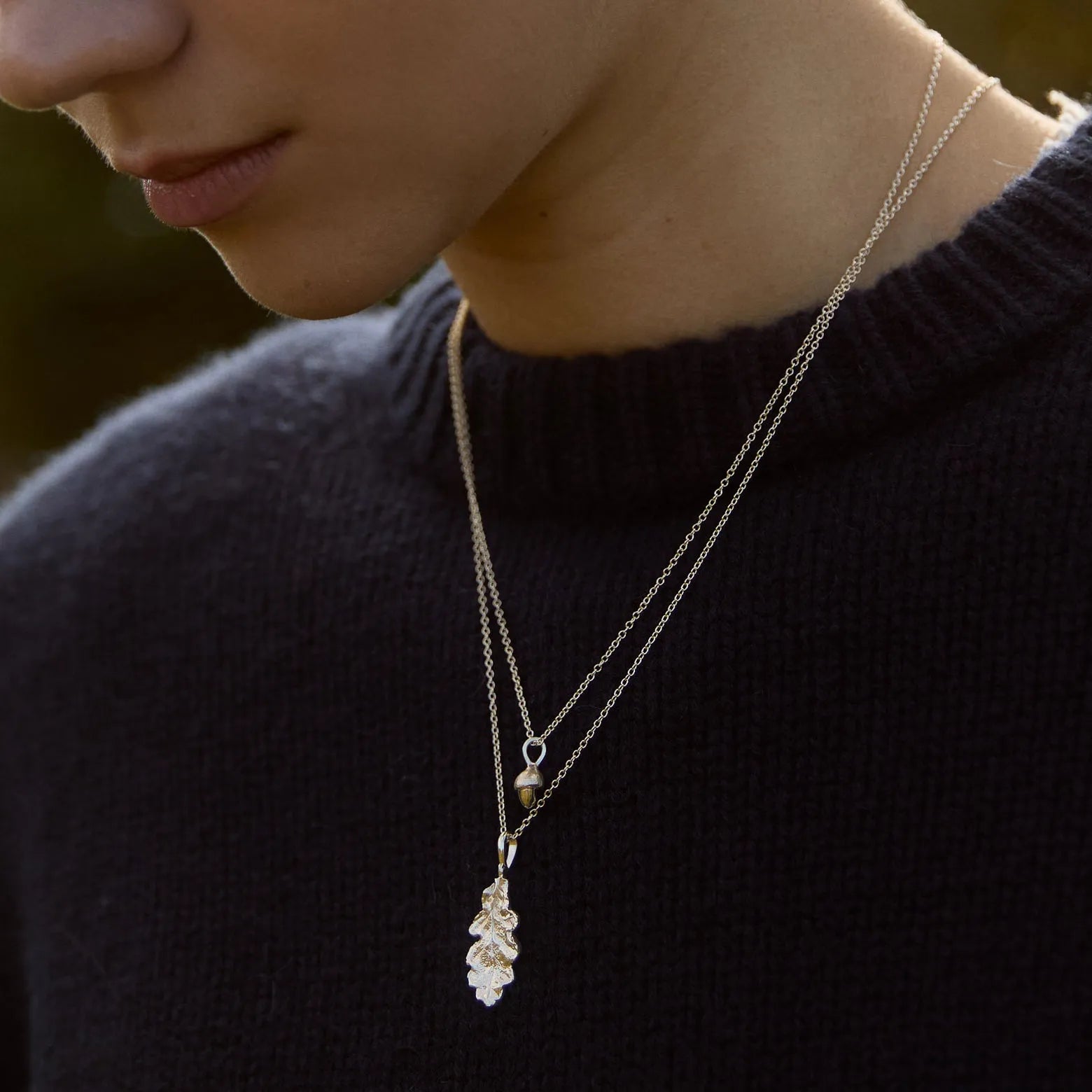 Close-up of a person wearing a leaf and acorn necklace against a navy jumper