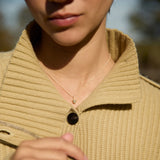 Close-up of a person wearing a gold necklace with a acorn pendant, outdoors.