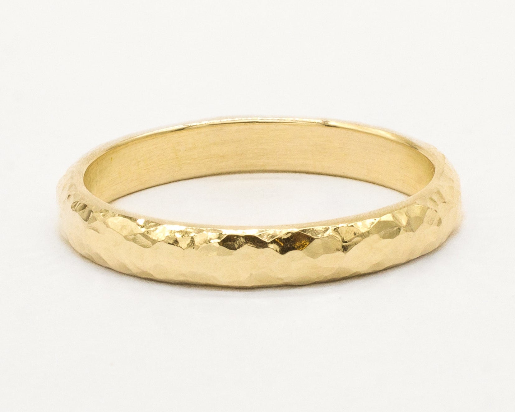 Gold ring with a dainty hammered surface on a white background