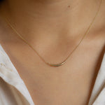 close up of curved gold necklace being worn by model wearing white shirt