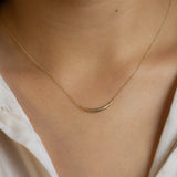close up of curved gold necklace being worn by model wearing white shirt