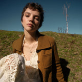 Woman in a brown jacket sitting outdoors with a clear blue sky and grassy hill in the background