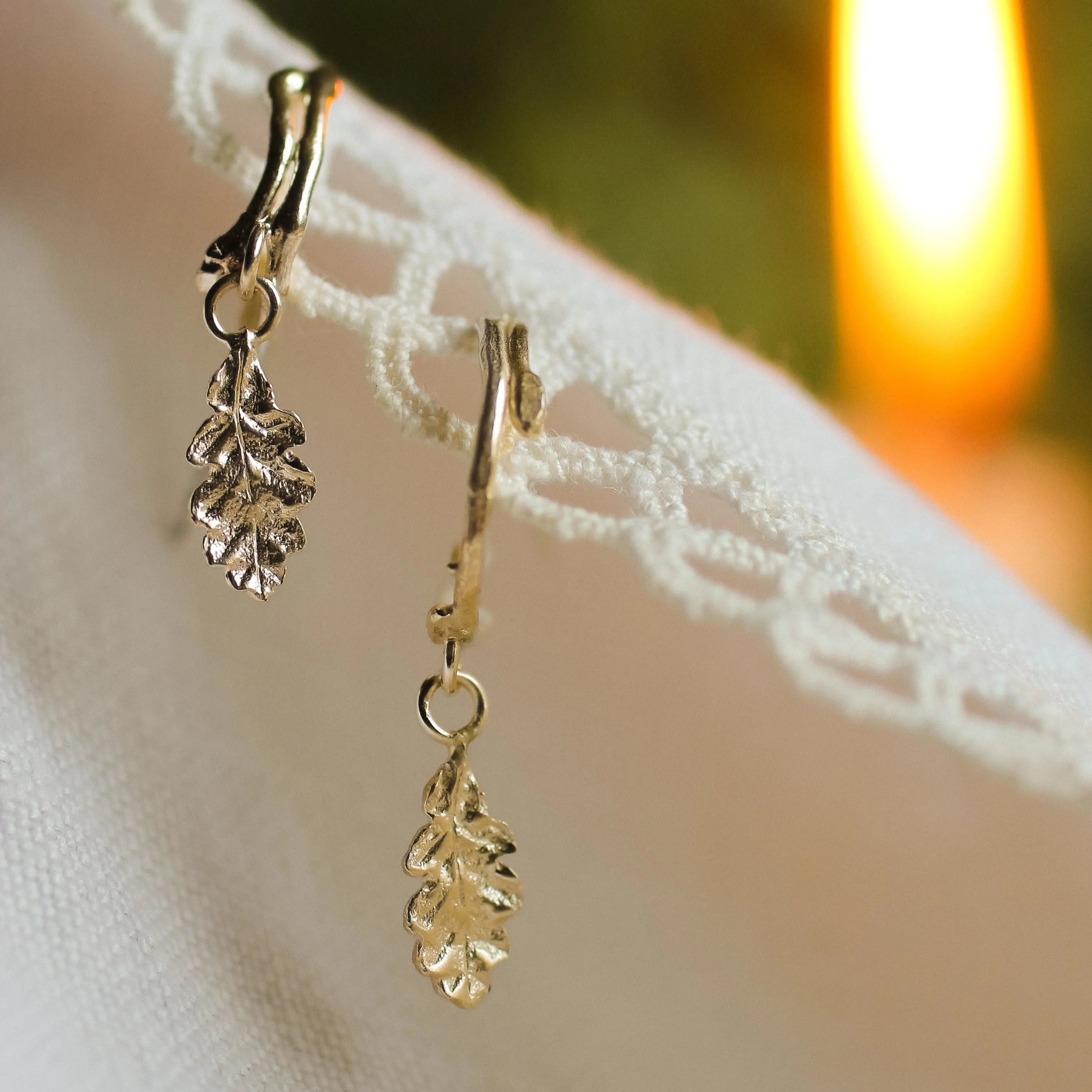 gold hoop earrings with twig detail and oak leaf pendants on fabric with candle