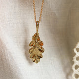 close up of solid gold oak leaf necklace pendant on neutral fabric